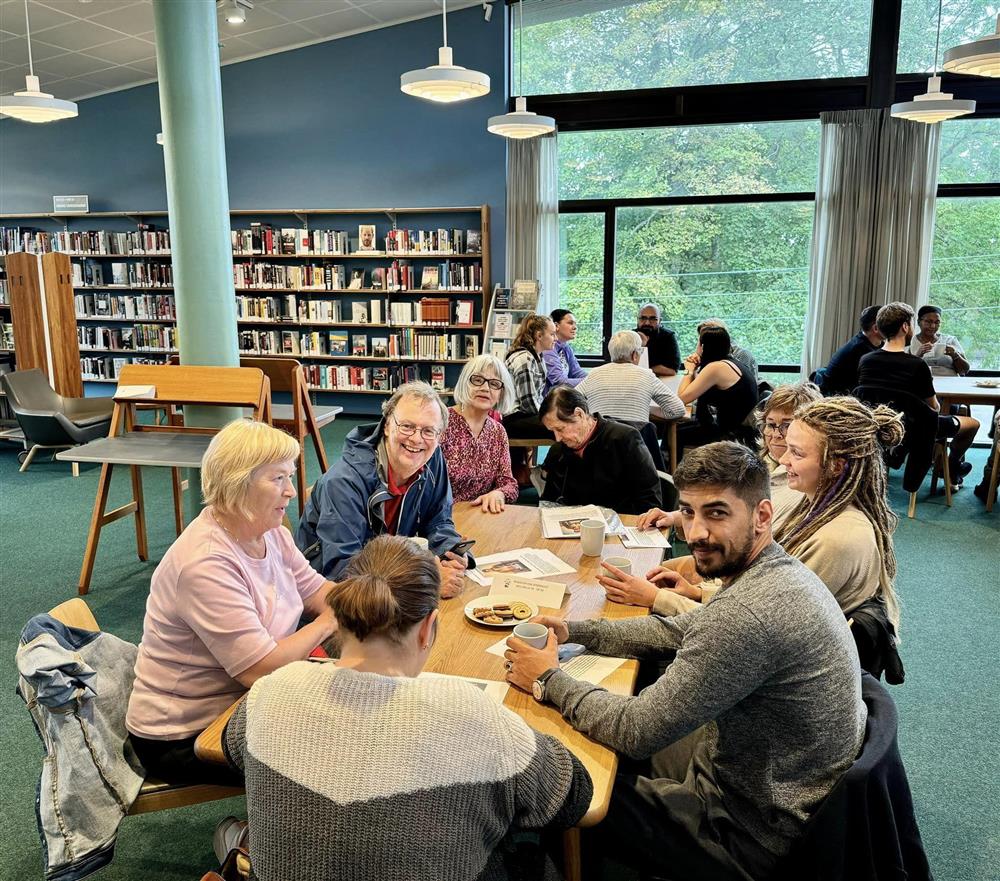 Mennesker fra ulike land samlet rundt et bord på biblioteket - Klikk for stort bilde